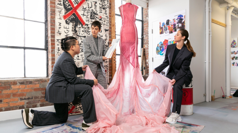 Three students working on a pink sheer dress on a dress form together